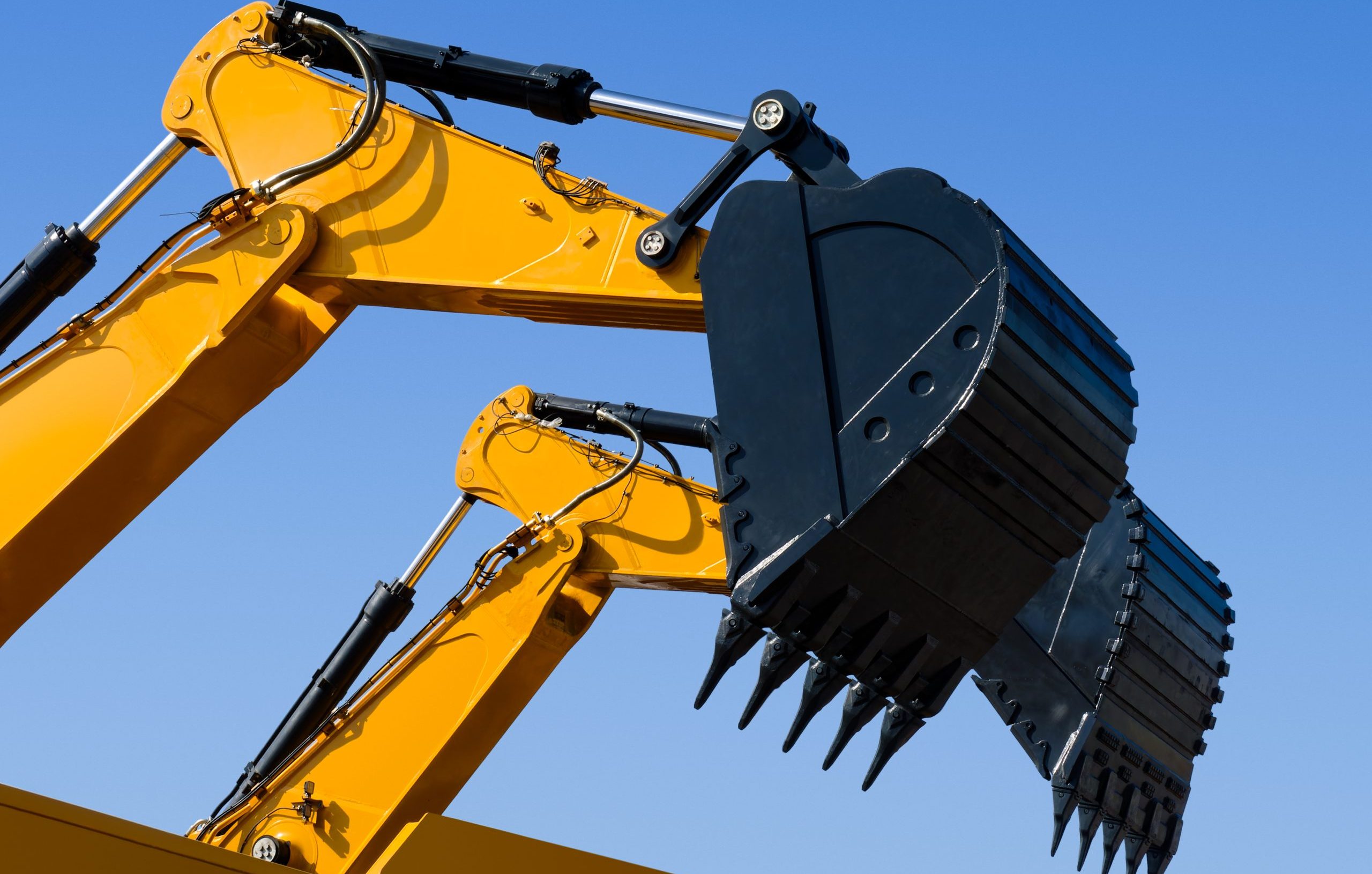 Scoop and hydraulic arm of an excavator, isolated on clear blue sky background, low angle perspective shot.