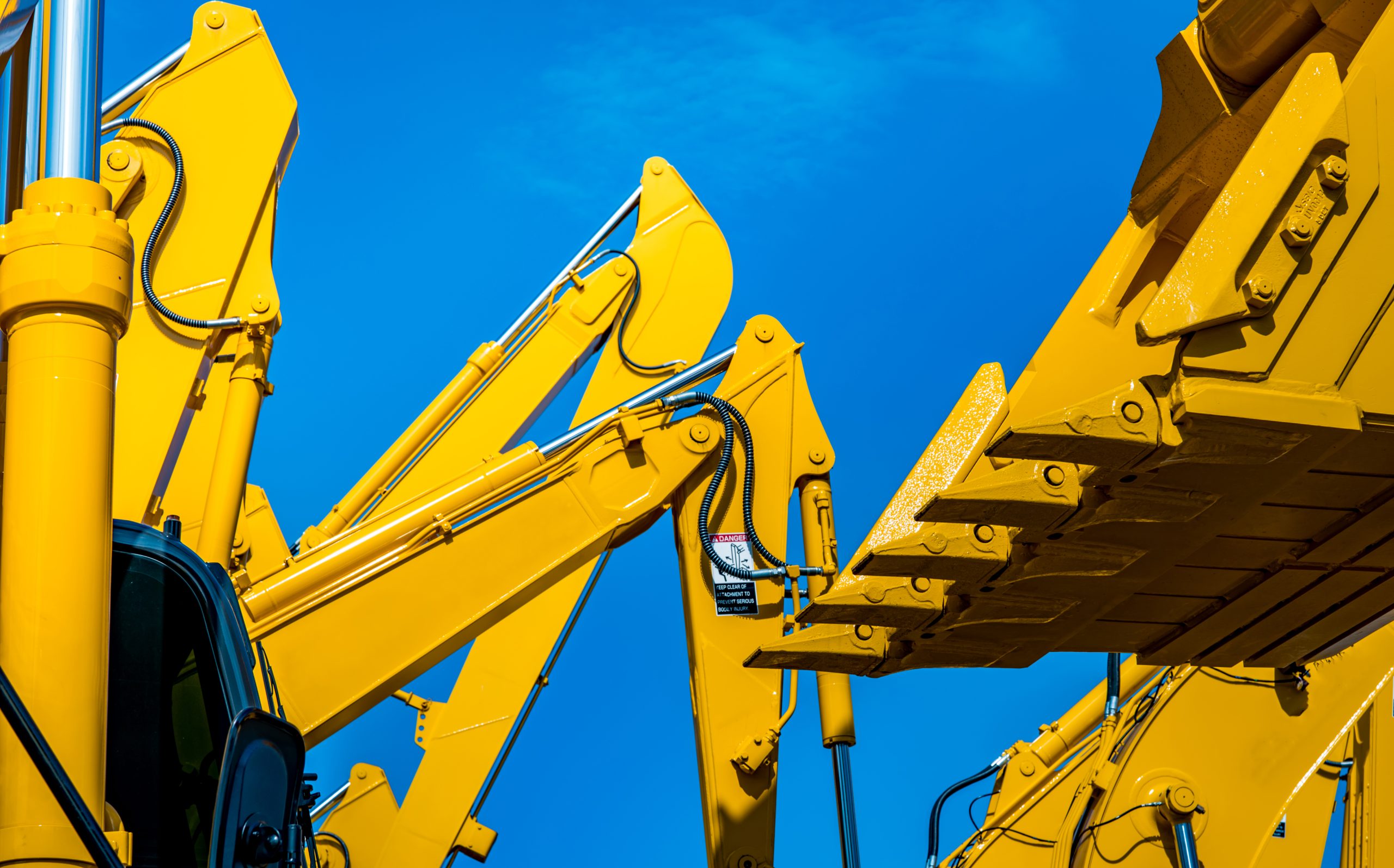 Yellow backhoe with hydraulic piston arm against clear blue sky. Heavy machine for excavation in construction site. Hydraulic machinery. Huge bulldozer. Heavy industry